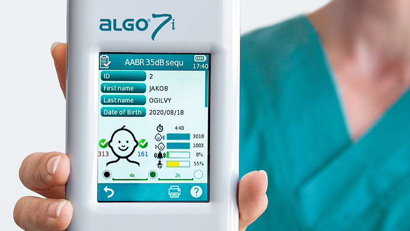 Clinician holding AABR device displaying newborn hearing screening results on screen.