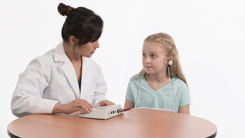 Clinician using a portable audiometry device to perform a hearing test on a young girl.