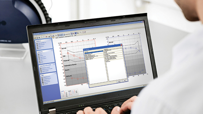Audiologist using fitting audiometer software on a laptop to analyze hearing aid fitting data.