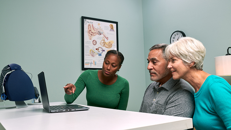 Audiologist reviewing hearing aid fitting results with older couple using Aurical system and PC-based audiometry.