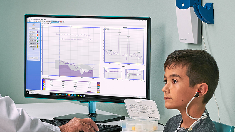 Child undergoing otoacoustic emissions test with Madsen Capella2 while test results are displayed on screen.