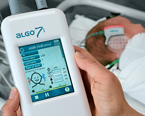 Clinician performing newborn hearing screening using an automated device in a neonatal care setting.