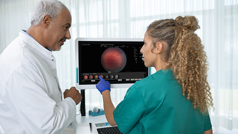 Healthcare professional using DataLink for RetCam Envision on a clinical workstation while a doctor observes, showcasing digital workflow integration for ophthalmic imaging and reporting.