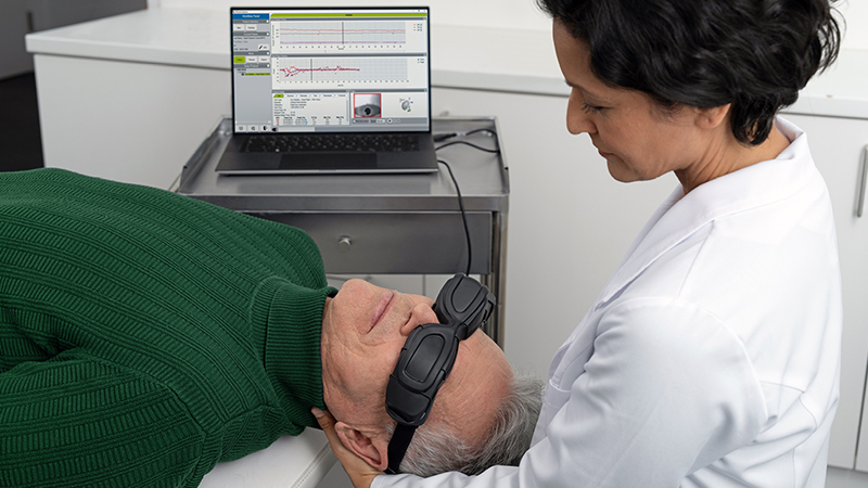 Clinician performing vestibular assessment using ICS Impulse goggles while patient lies down, with real-time eye movement data displayed on a laptop.