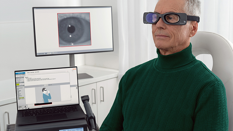 Patient wearing ICS Impulse goggles during vestibular testing, with eye movement data displayed on monitor and instructions on laptop.
