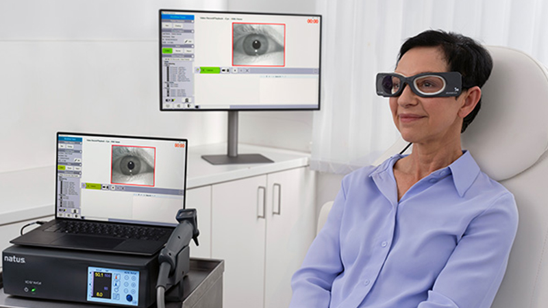 Patient wearing ICS Impulse goggles during vestibular testing, with eye movement tracking displayed on monitor screens.