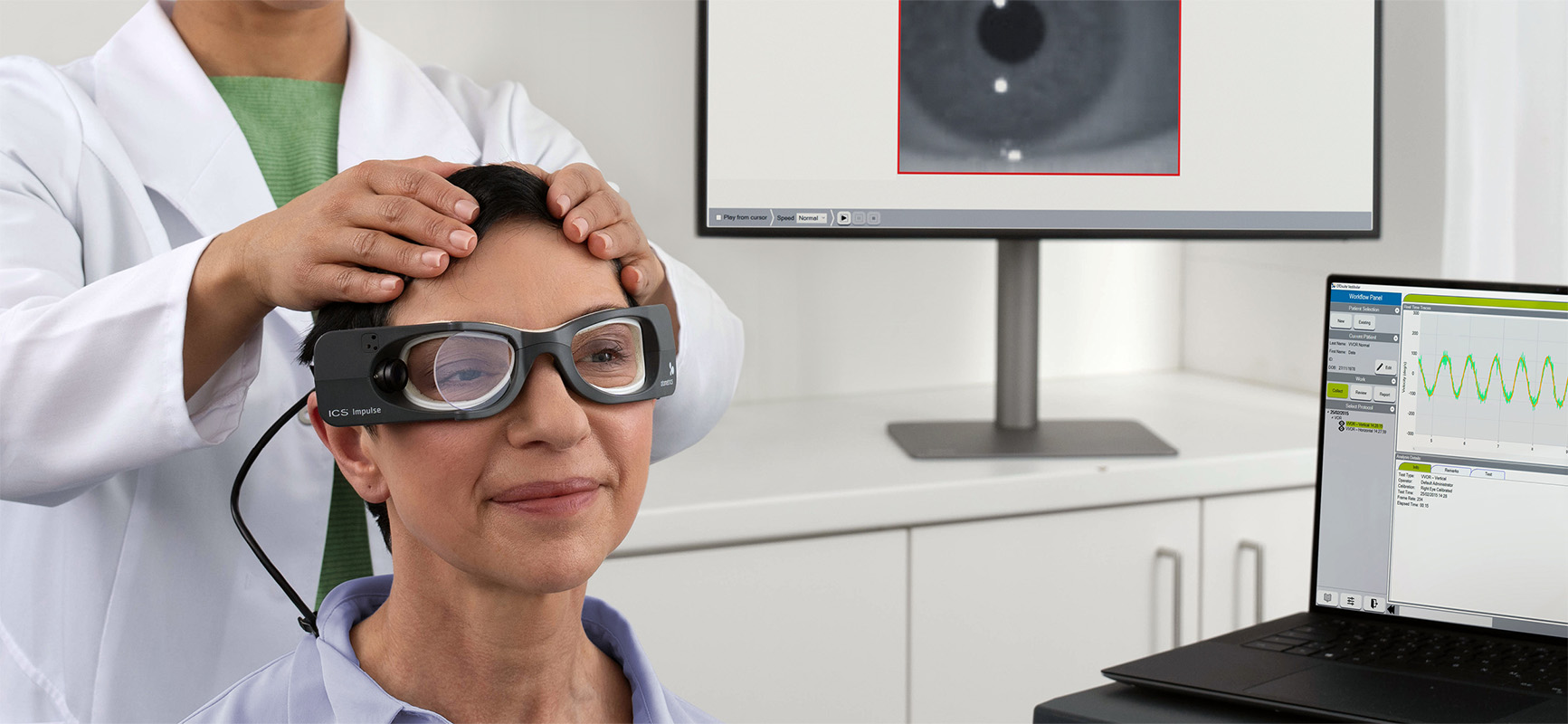 Clinician performing a head impulse test using ICS Impulse goggles, with real-time eye tracking data displayed on connected monitors.