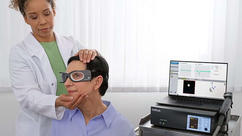 Clinician guiding a patient through a head impulse test using ICS Impulse goggles, with real-time vHIT data shown on the connected laptop.