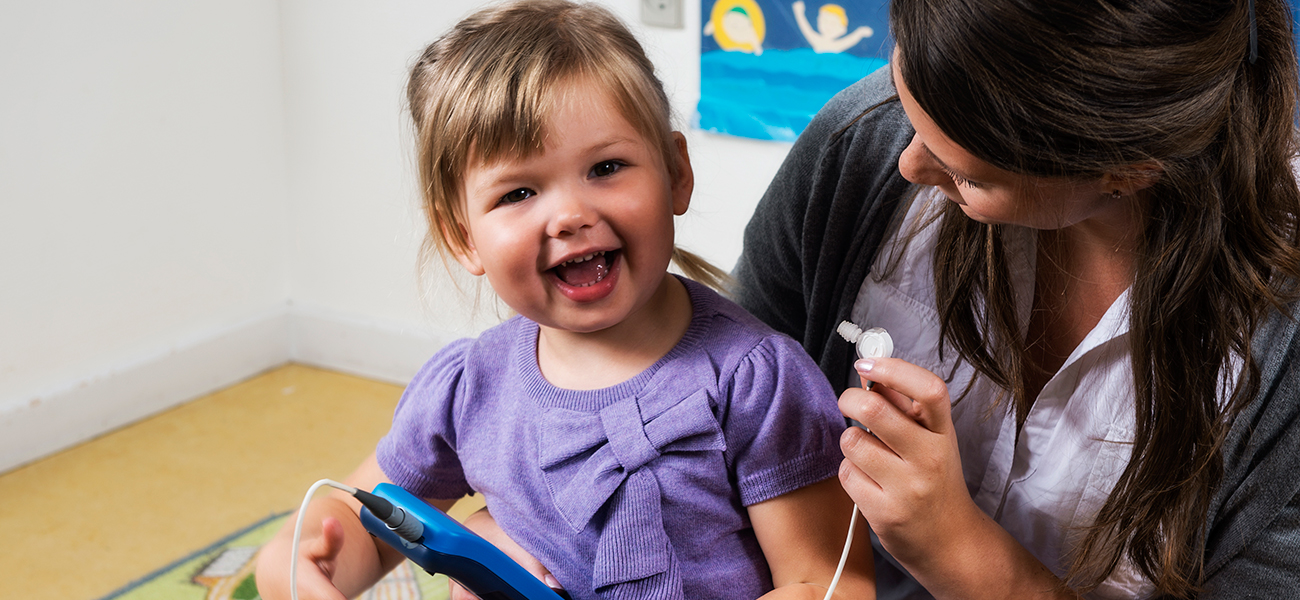 Clinician using Madsen Alpha Pediatric Hearing Screener for OAE testing on a smiling preschool child.