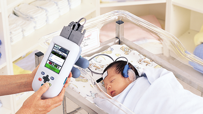 Newborn undergoing hearing screening with handheld device for data collection and management.