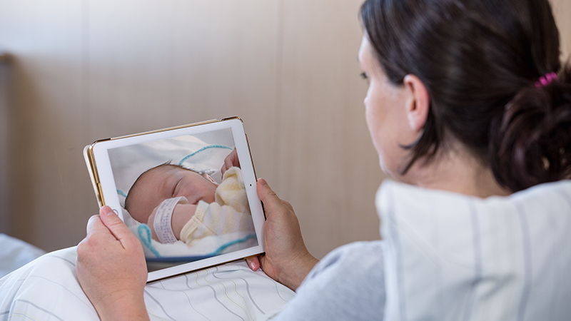 Mother watching a live video stream of her newborn in NICU on a tablet device.
