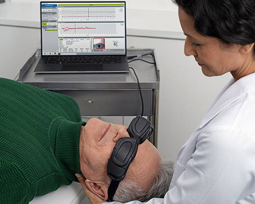 Audiologist performing a vestibular assessment on a senior patient using video goggles and diagnostic software.