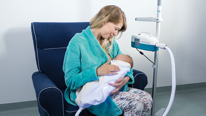 Mother using neoBLUE blanket LED Phototherapy System for neonatal jaundice treatment.